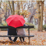 公園のベンチで傘の下のカップル